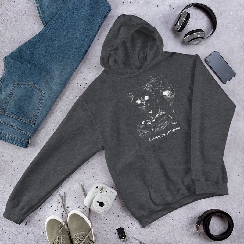 Dark grey hoodie printed with a white line drawing of a cat on a stack of papers and the line “I teach, my cat grades”