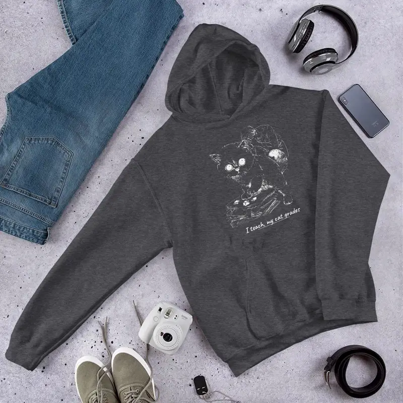 Dark grey hoodie printed with a cat on a stack of papers and the line “I teach, my cat grades”